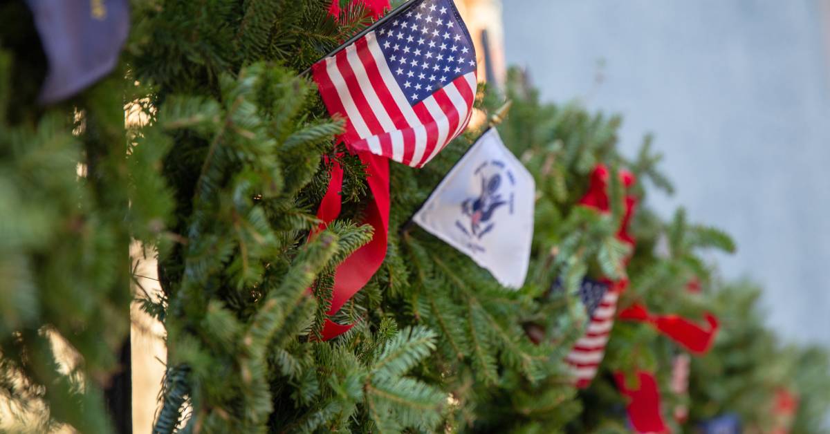 A fence decorated with Christmas and American decorations, including a reef and American and military service stick flags.