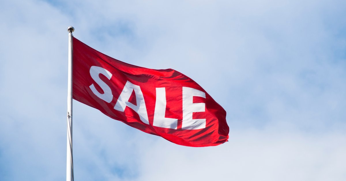 A large red flag on a flagpole flaps in the breeze. The word SALE appears on it in big white letters.