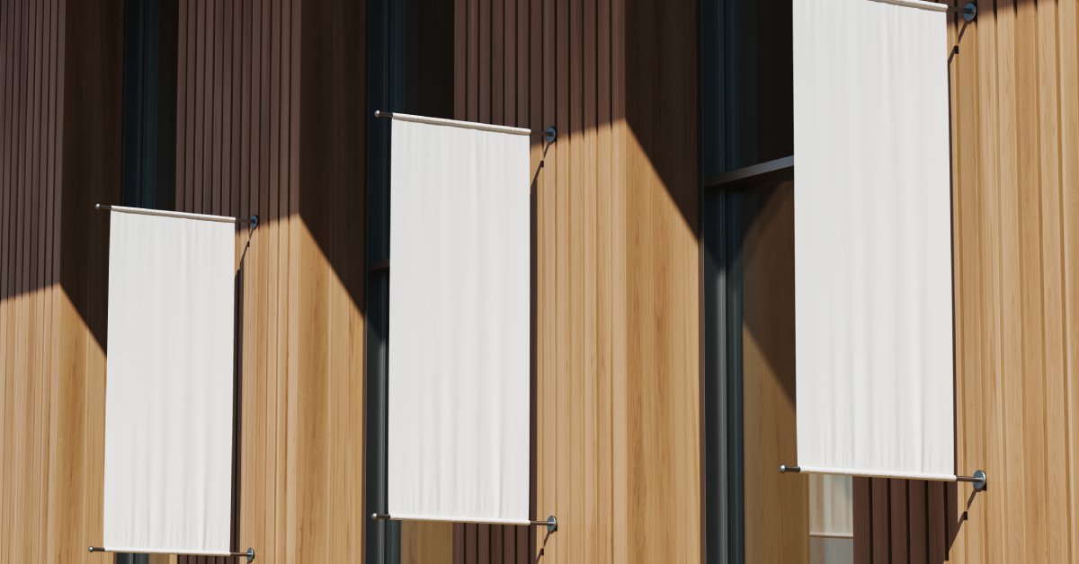 Three large white blank vertical street banners hanging in a row from a wood-slatted building's exterior.