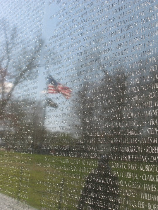 A picture of a American Flag seen through the reflection of a veteran memorial wall monument