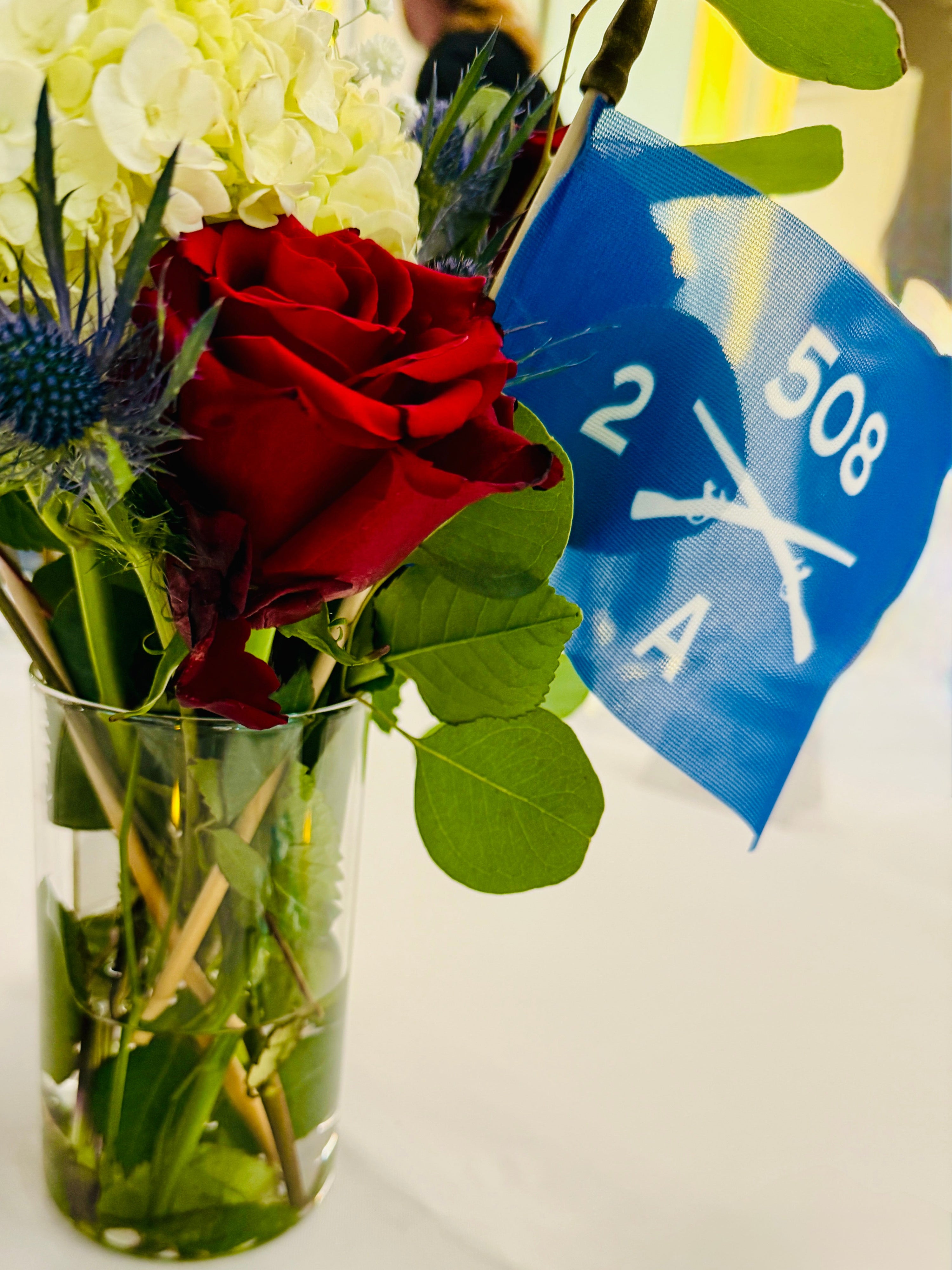 A picture of a A 2 508 PIR 4 x 6 inch stick flag in a table centerpiece along with a US Stick flag and flowers.